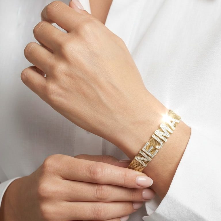 Femme portant un bracelet en maille dorée personnalisé avec le prénom Nejma en lettres strass. Création sur-mesure Rêve Étoilé.