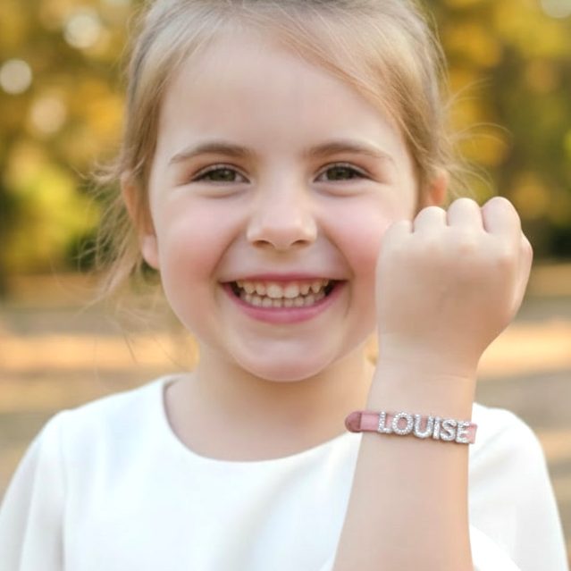 Avis client Rêve Étoilé avec une petite fille souriante portant un bracelet personnalisé en cuir rose au prénom de Louise